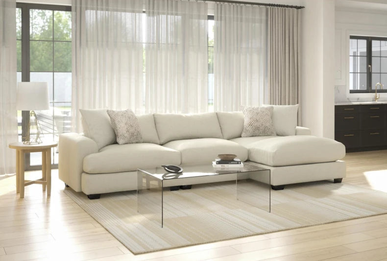 Beige sectional sofa in a living room with light wood flooring and large windows.