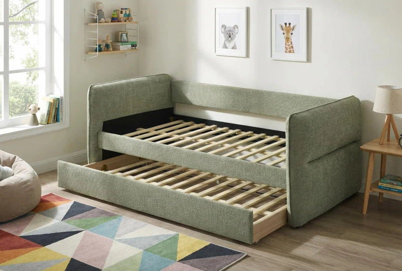 Green upholstered sofa bed with a wooden slatted frame in a room with a rug and shelves.
